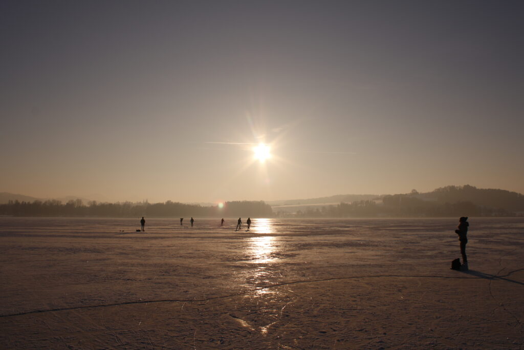 Eislaufende Menschen auf dem Tachinger See.